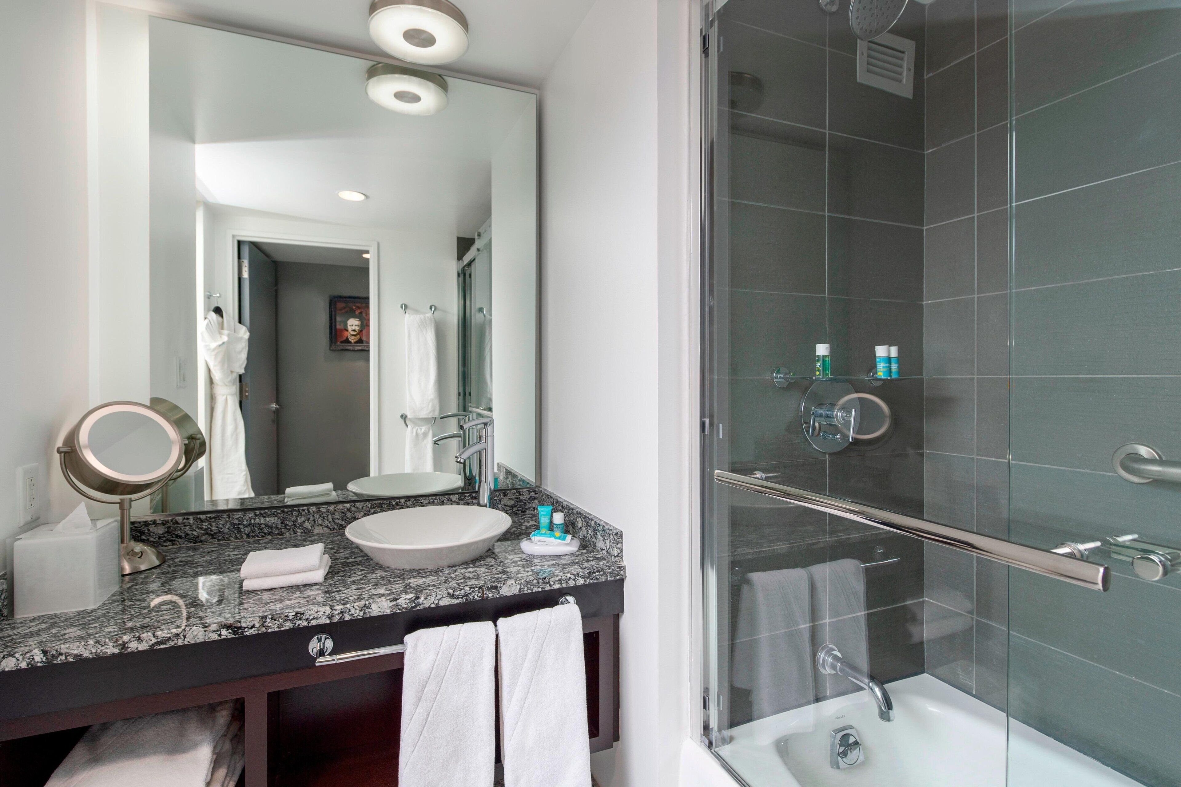 A modern bathroom with a granite countertop, a large mirror, a glass shower enclosure, and a white sink.