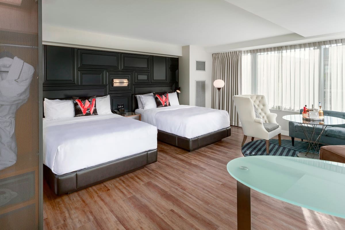 Een hotelkamer met twee bedden, een zithoek met een glazen tafel en uitzicht op het omliggende landschap door grote ramen.