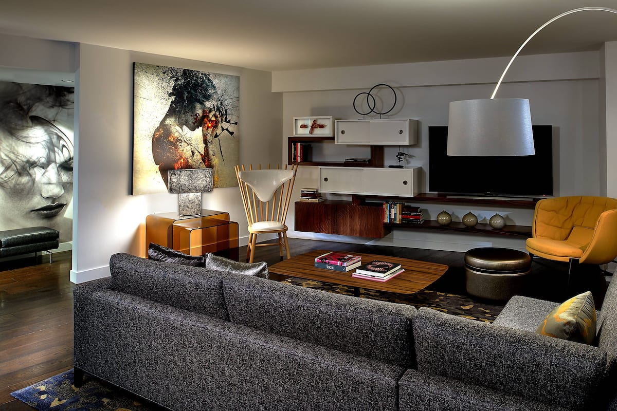 Een moderne woonkamer met een grijze bank, een houten salontafel, een gele fauteuil, een groot schilderij en een flatscreen televisie.