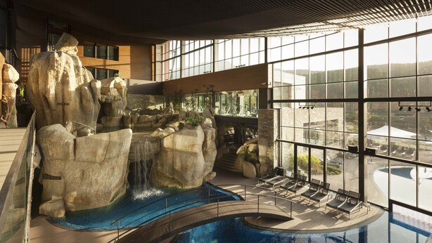 An indoor pool with a waterfall feature, lounge chairs, and large windows offering views of the surrounding area. - H2otel Congress & Medical Spa (Covilhã)