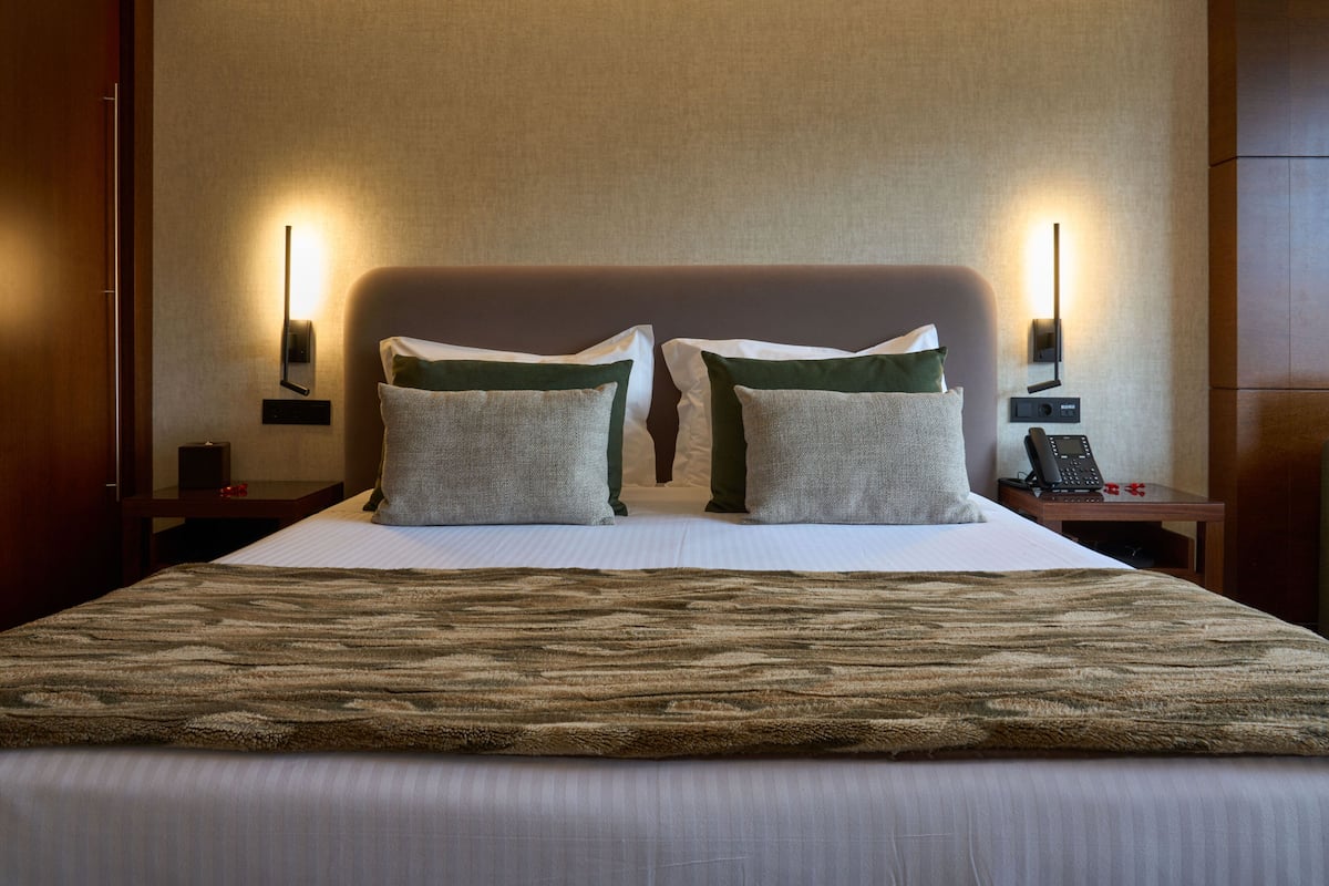 A hotel room with a large bed, two bedside tables, a wall-mounted phone, and a nightstand with a lamp.