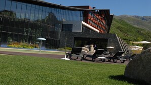 A modern building with a glass facade, outdoor seating area with lounge chairs, and a view of the surrounding landscape. - H2otel Congress & Medical Spa (Covilhã)