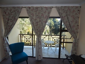 A room with a blue chair, a small round table, and a balcony with a railing. - Elephant Lake Hotel (St. Lucia)