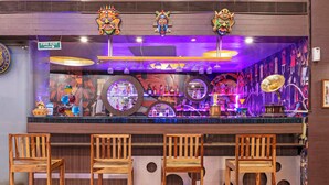 Eine Bar mit Holzsesseln, einem Feuerschutzschild und bunten Masken an der Wand.