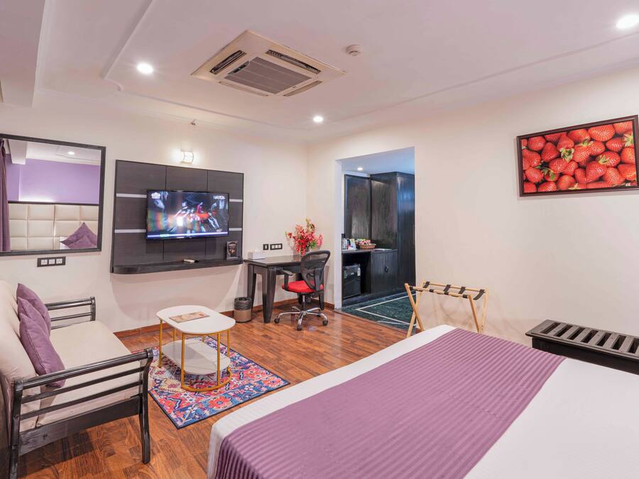 Quarto de hotel moderno com uma cama, uma escrivaninha, uma cadeira, uma TV e um banheiro visível através de uma porta aberta.