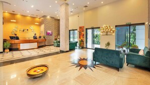 Eine Hotelhalle mit einer Rezeption, grünen Sofas, einem fußbodenhohen Sonnendesign und großen Fenstern.