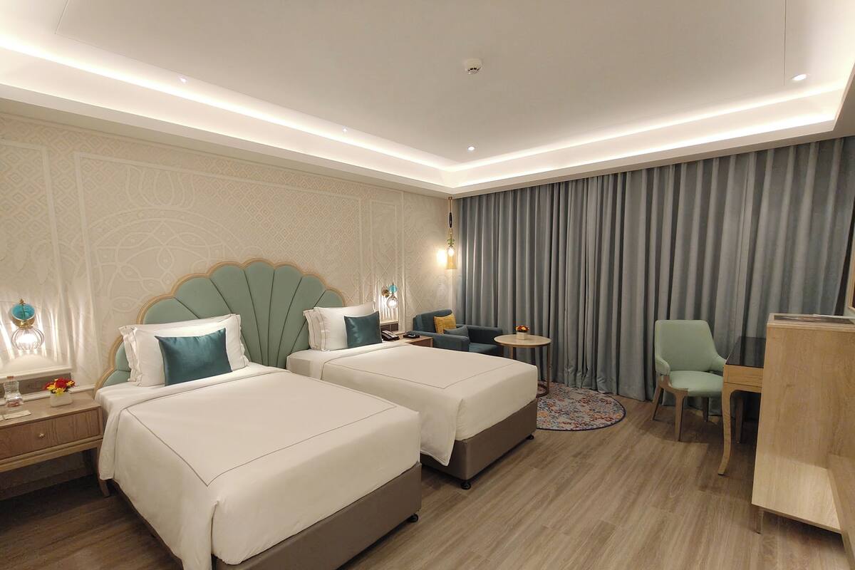 A hotel room with two beds, a desk, a chair, a small table, and a curtain.