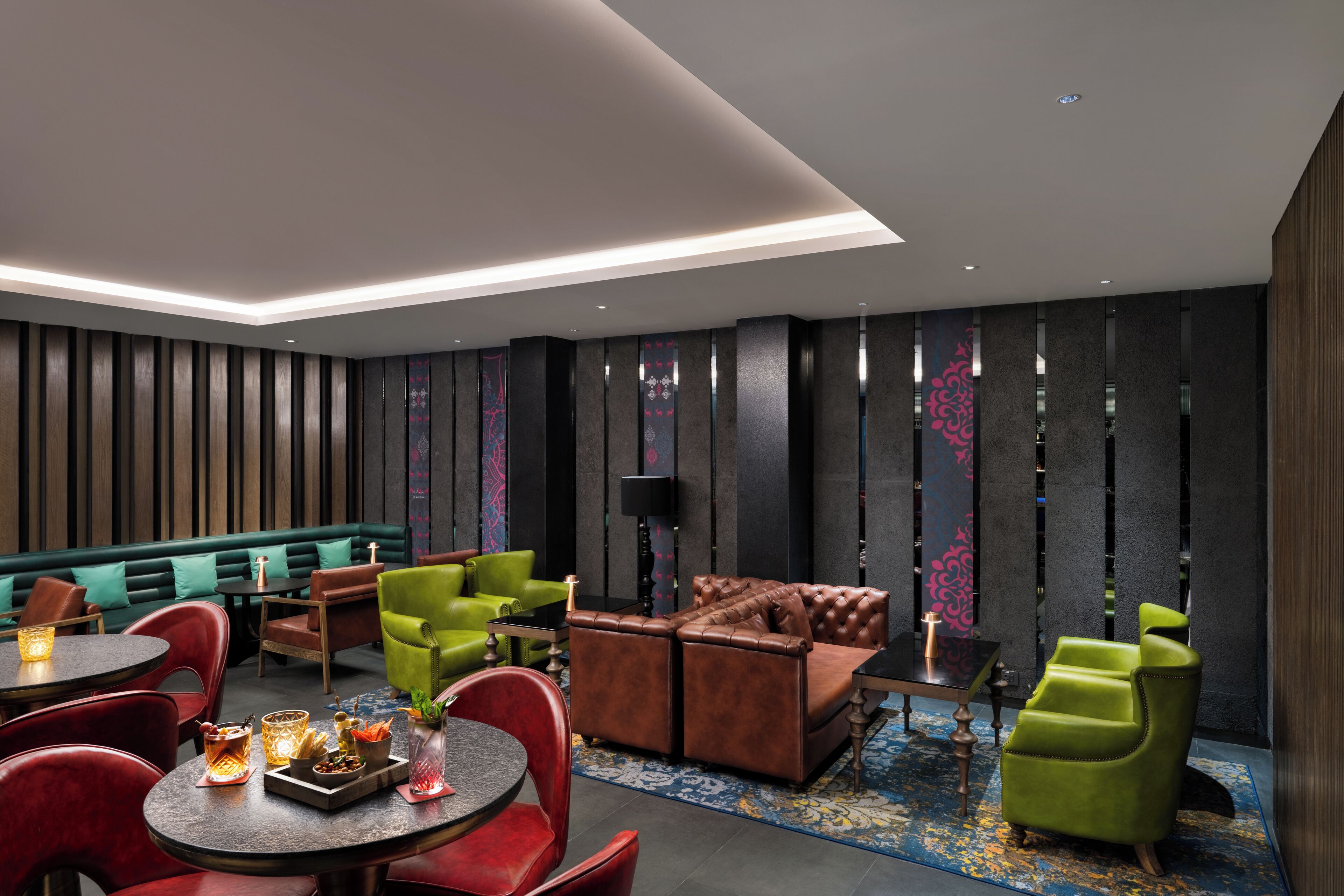 A modern lounge area with leather sofas, green chairs, and a round table with drinks.