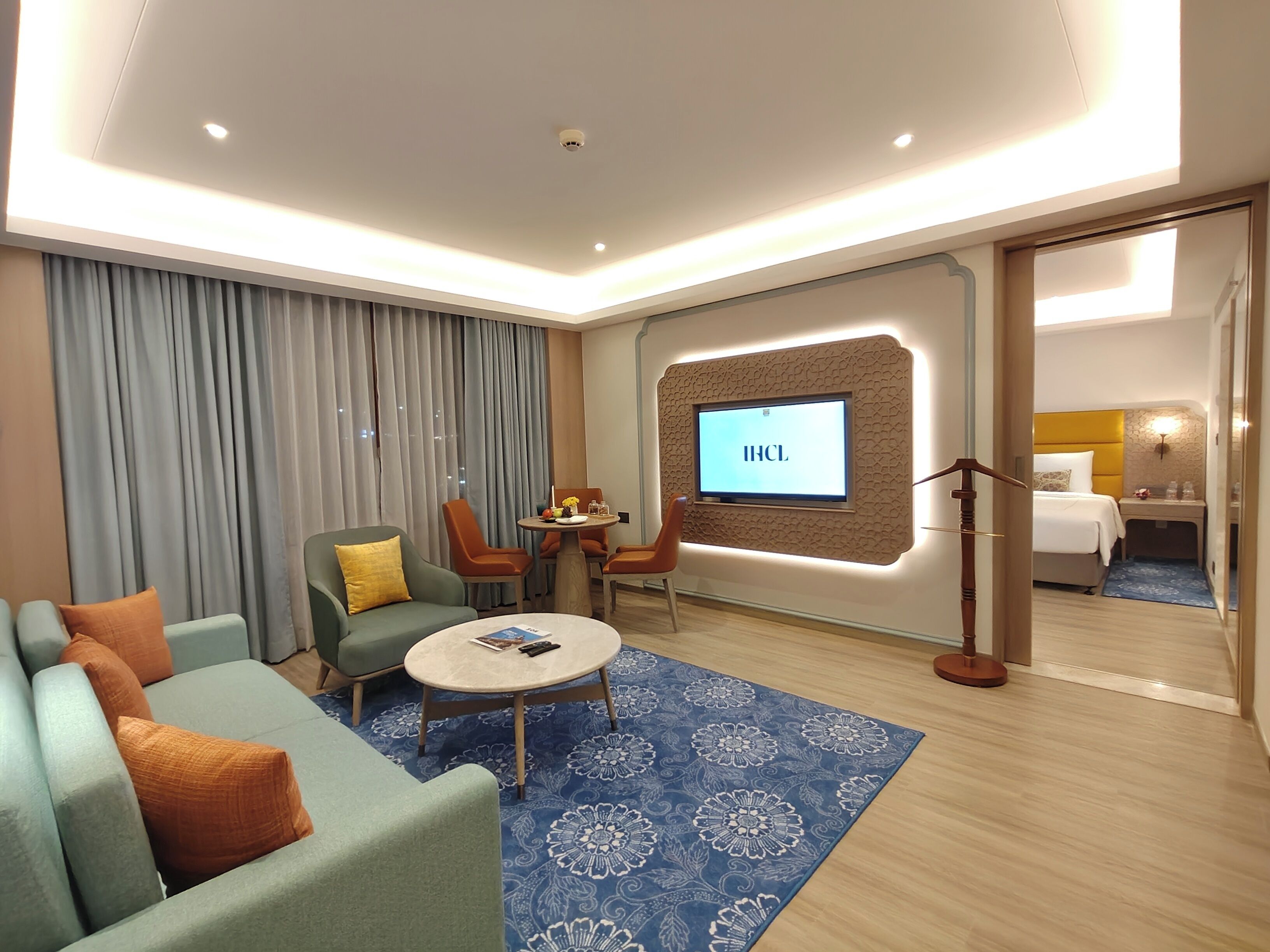 Une chambre d’hôtel moderne, dotée d’un canapé, de fauteuils, d’une table basse, d’un téléviseur fixé sur un mur texturé et d’un lit avec une tête de lit.
