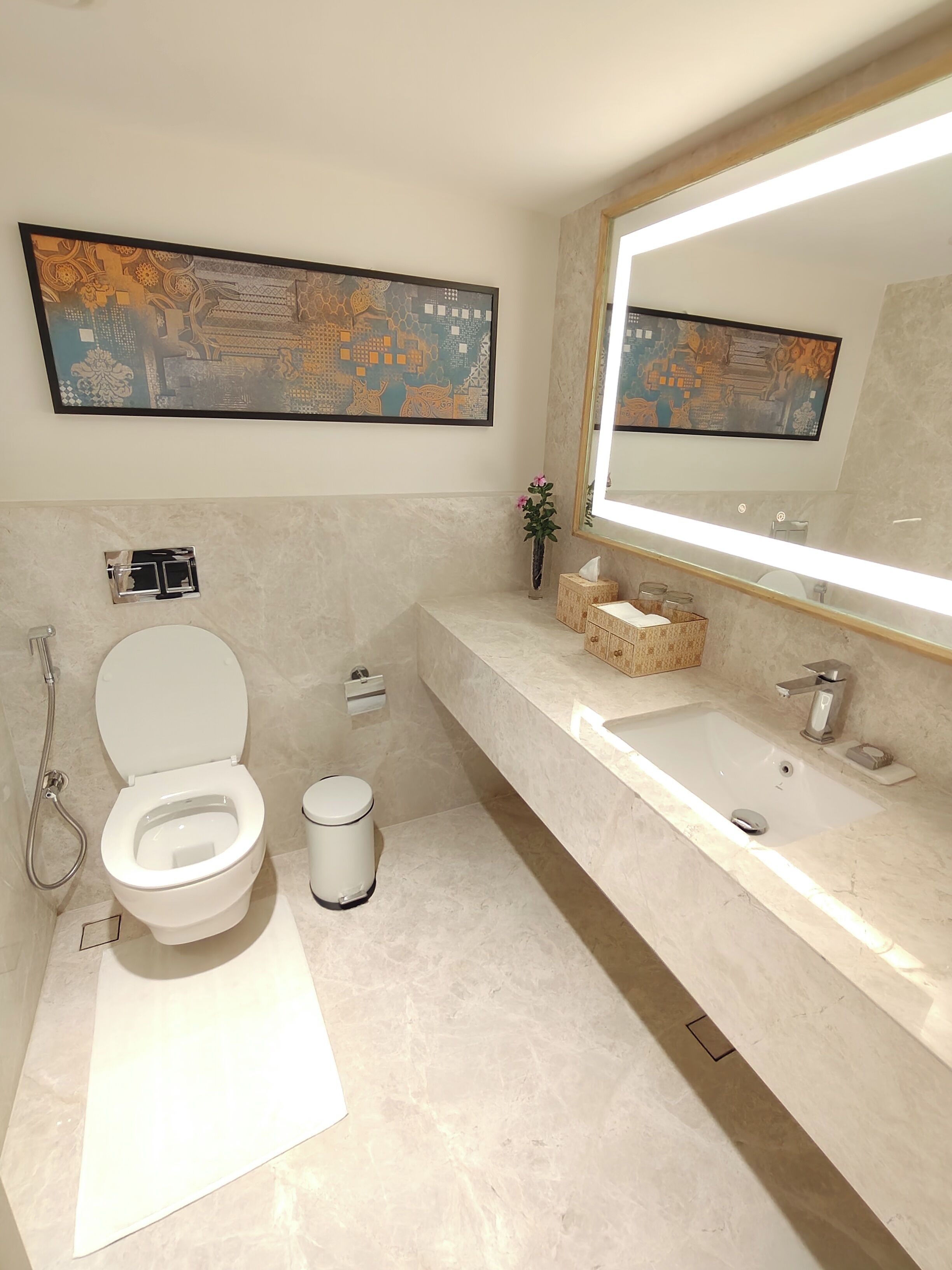 Ein modernes Badezimmer mit Toilette, Bidet und Waschbecken. Über dem Waschbecken befinden sich zwei große Spiegel und an der Wand ein dekoratives Bild.