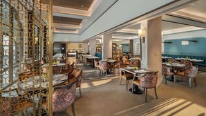 A spacious dining area with multiple tables and chairs, a decorative partition, and a view of a blue wall in the background. - Ekante Bliss IHCL SeleQtions  (Tirupati)