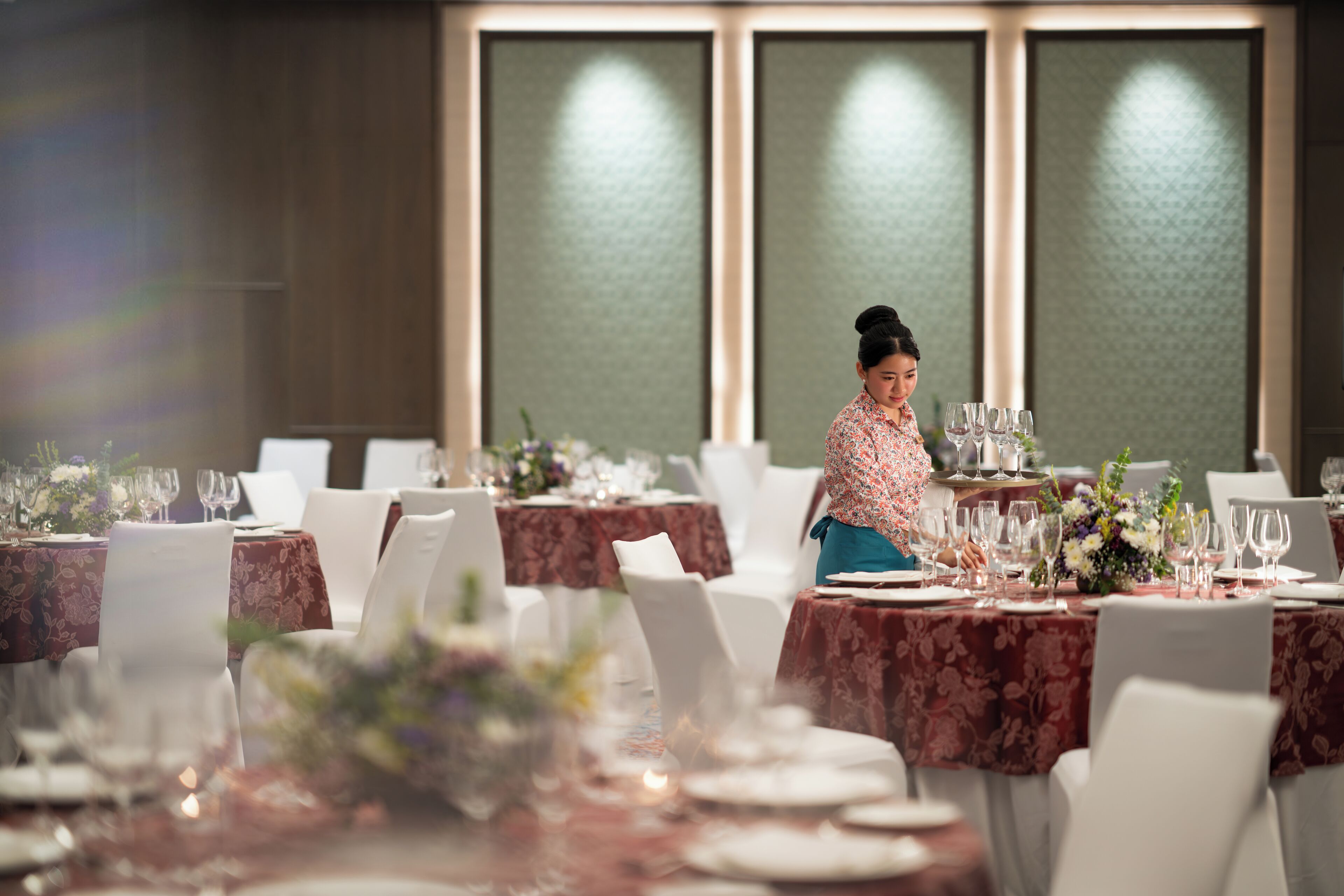 A dining area with tables set for a meal, each with a floral centerpiece and white chairs.