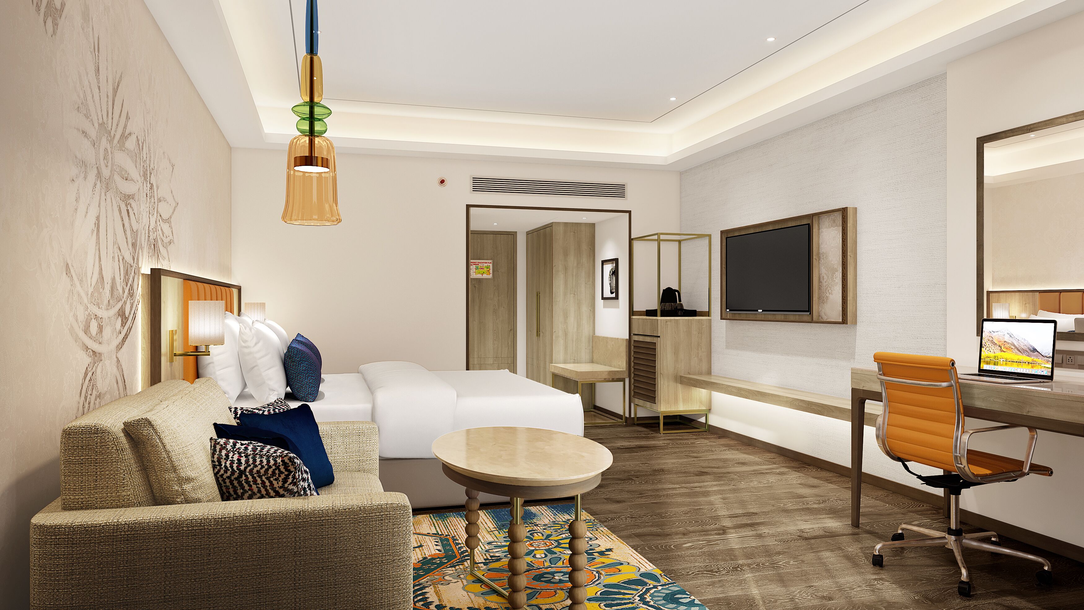 A modern hotel room with a sofa, a small round table, a desk with a chair, a TV, and a wardrobe.