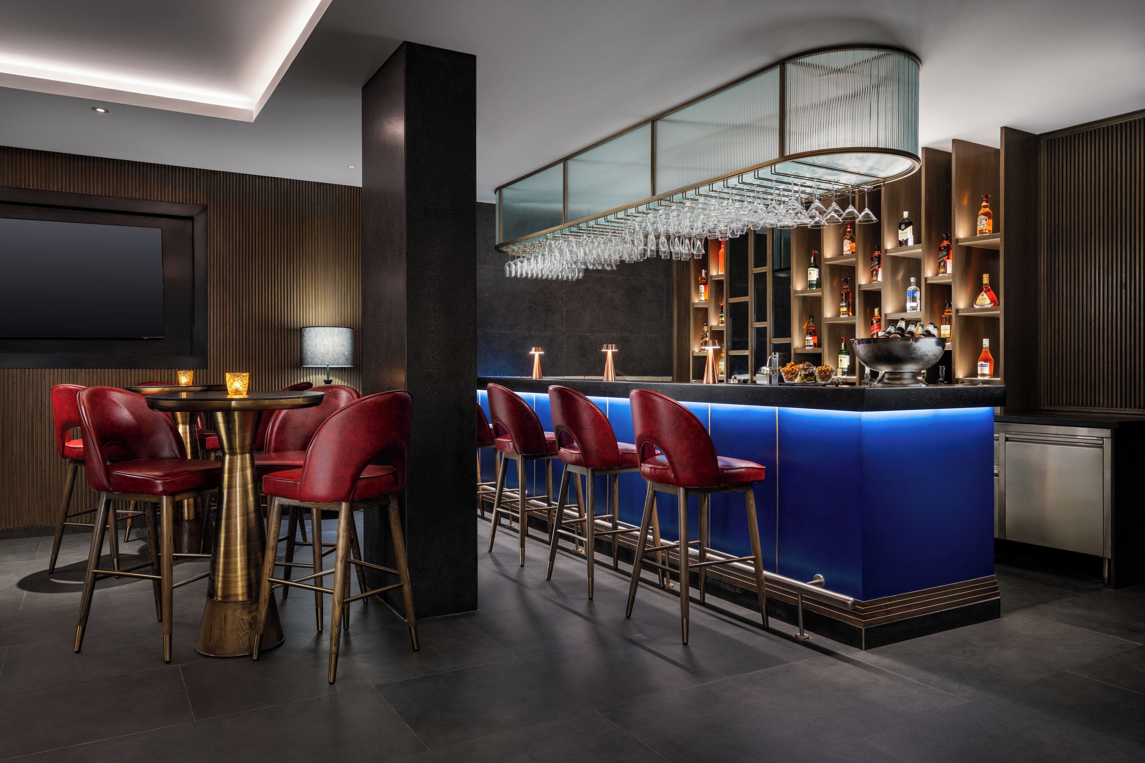 Un espace bar moderne avec des tabourets rouges, un comptoir bleu et un présentoir à bouteilles.