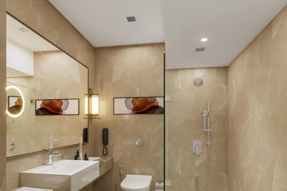 A modern bathroom with a large mirror, two sinks, a toilet, and a glass-enclosed shower area.