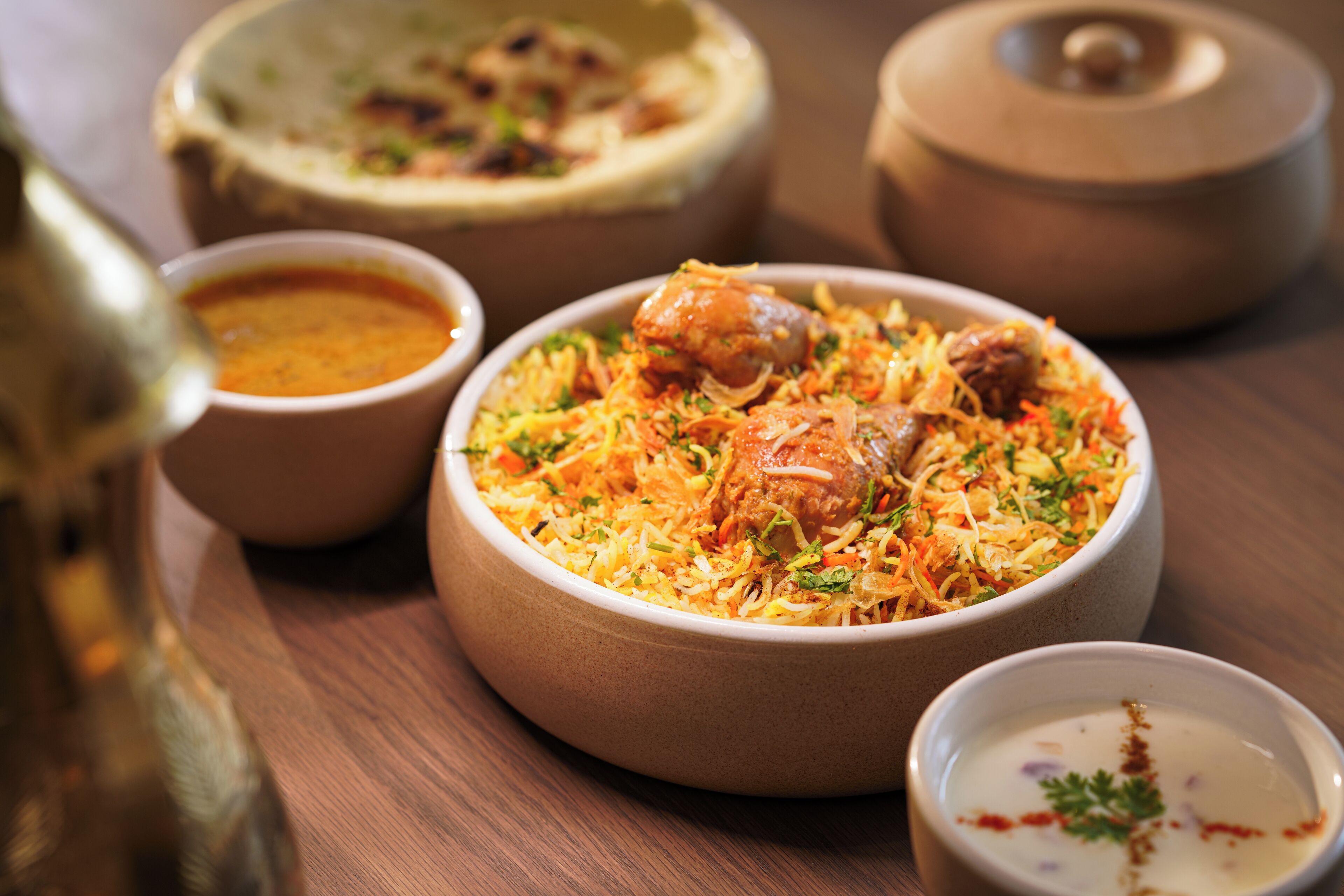 A table with a bowl of biryani, a bowl of raita, and a pot of soup.