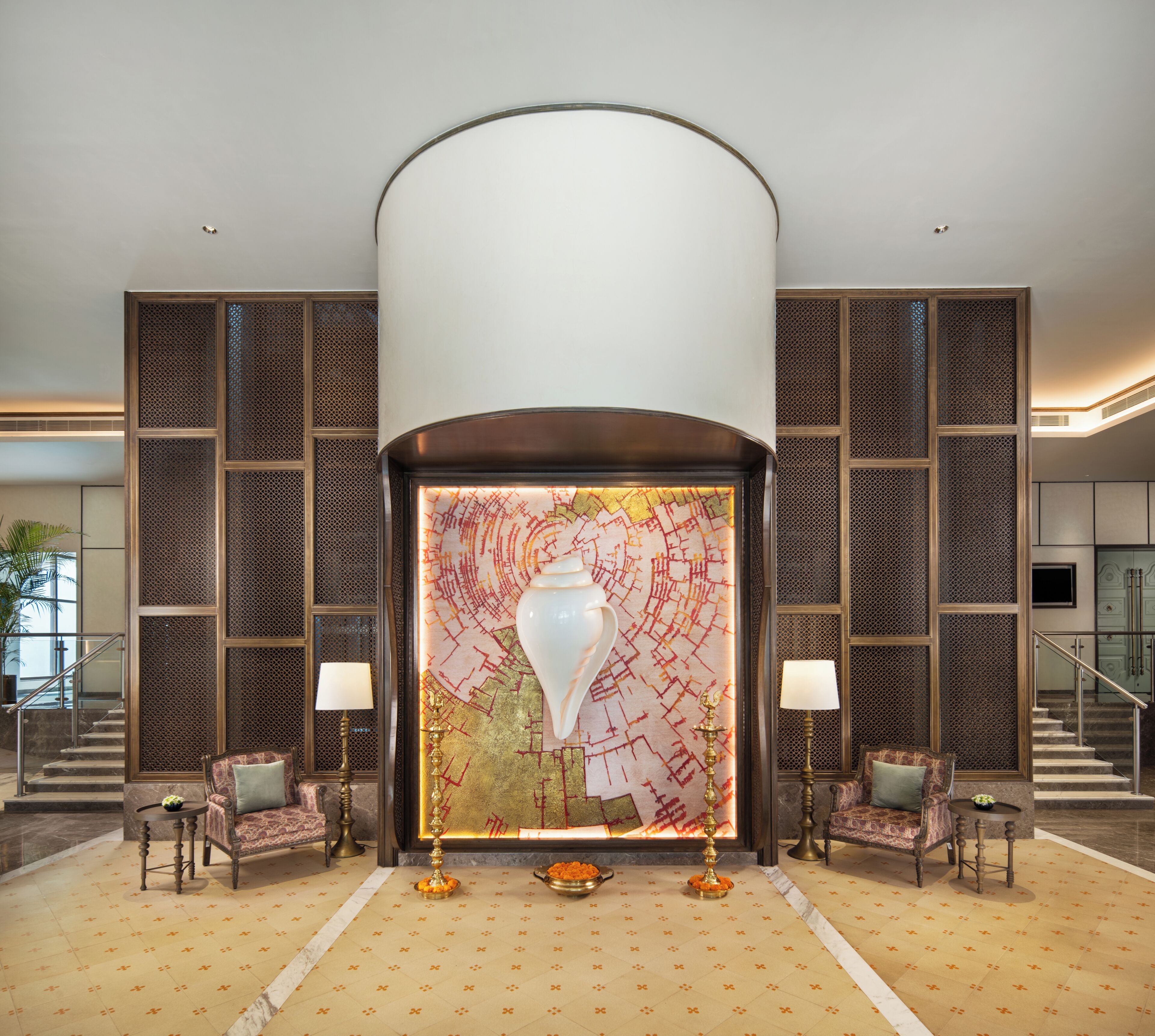 A lobby with a large decorative wall, two sofas, a floor lamp, and a staircase.