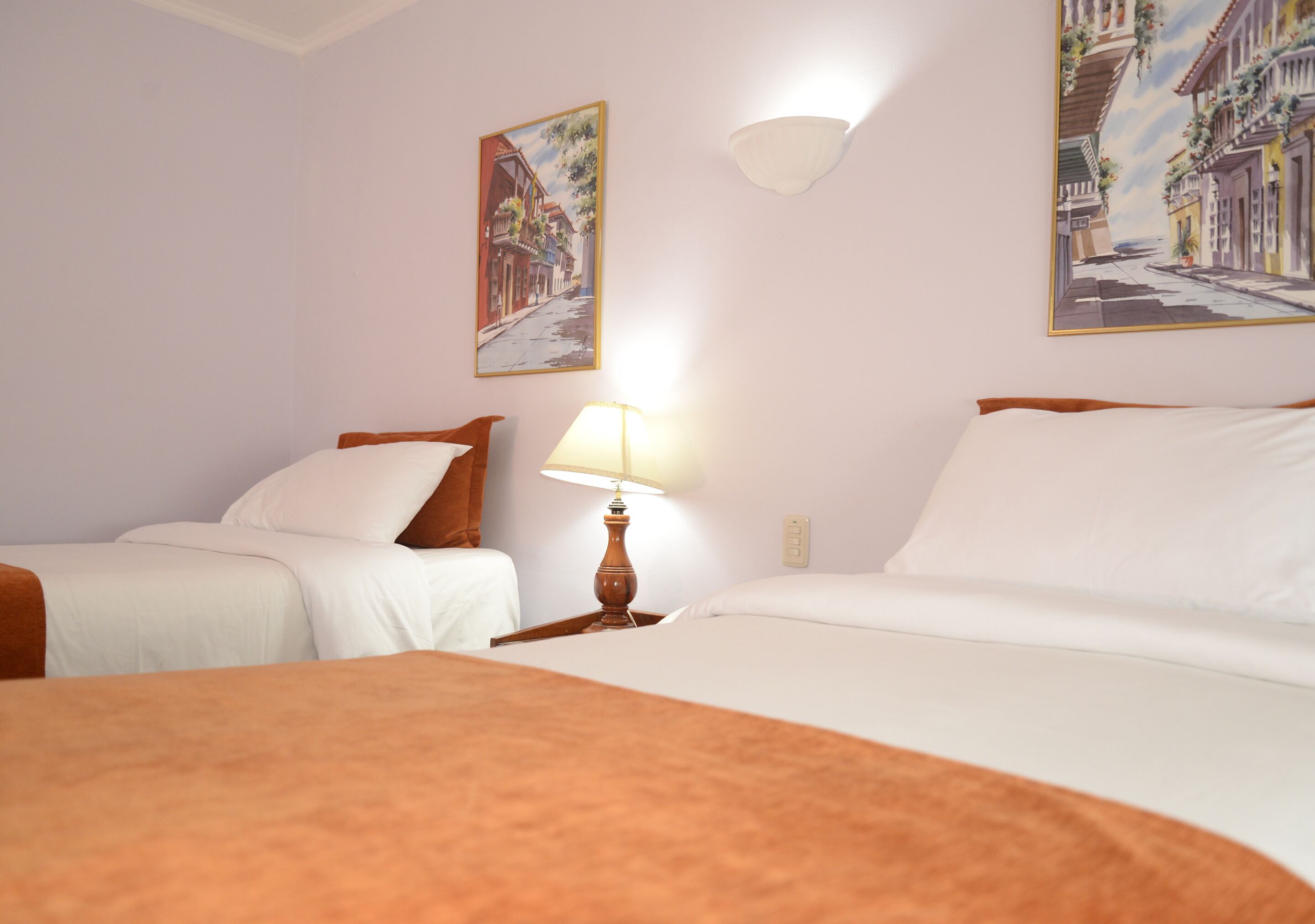 Une chambre d’hôtel avec deux lits, une table de chevet avec une lampe et deux tableaux accrochés au mur.