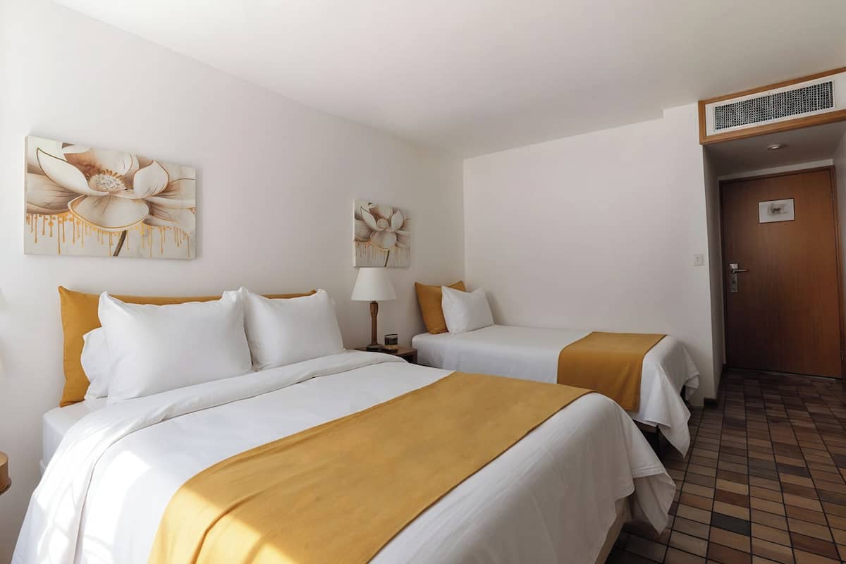 A hotel room with two beds, a nightstand with a lamp, and artwork on the walls.