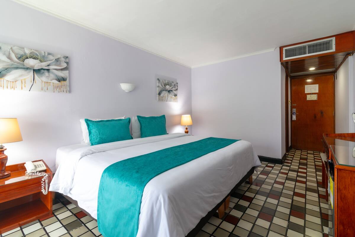 A hotel room with a bed, a nightstand with a phone, two wall-mounted lamps, and a door with a vent.