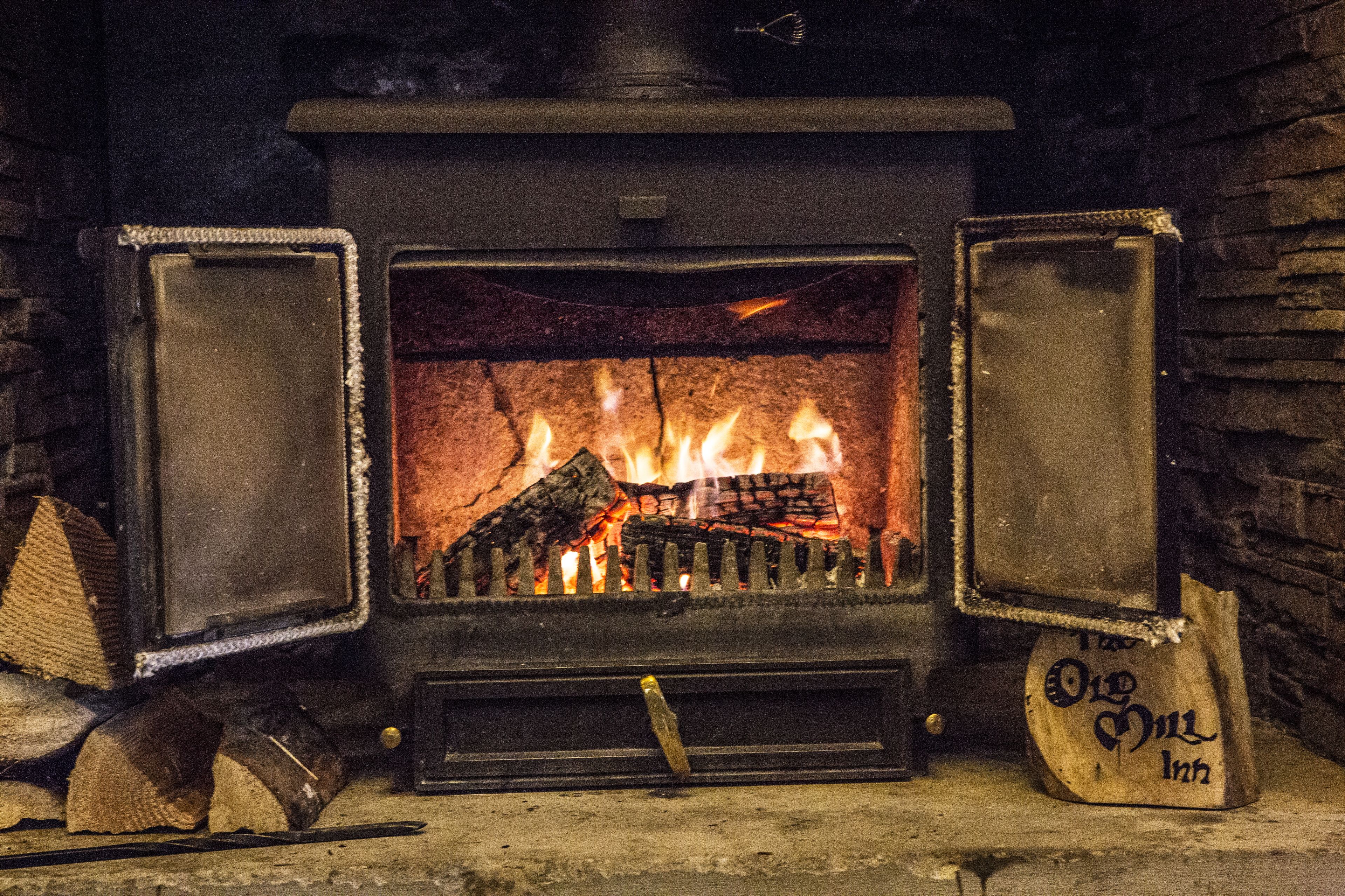 A wood-burning stove with open doors, logs inside, and a sign on the right.