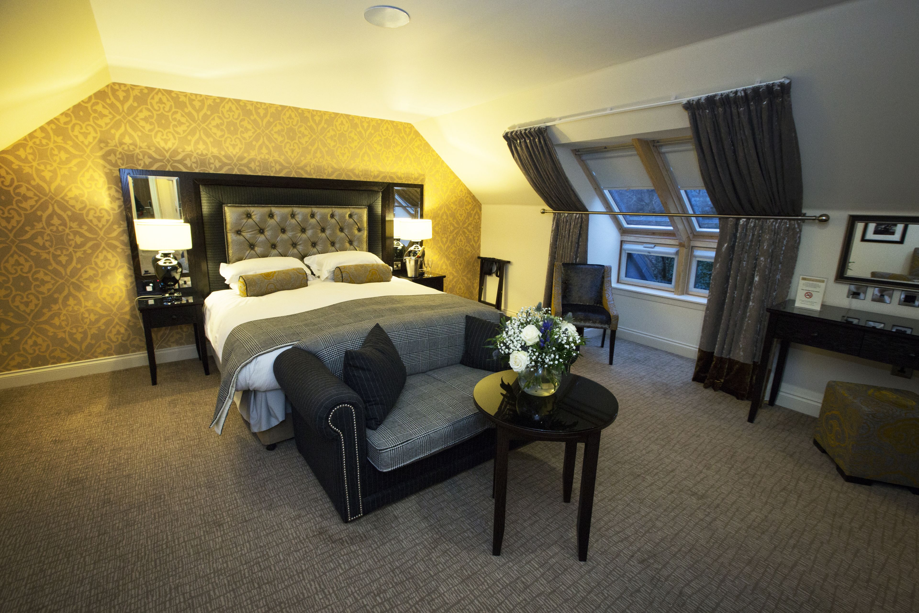 A hotel room with a large bed, a sofa, a desk, and a window with curtains.