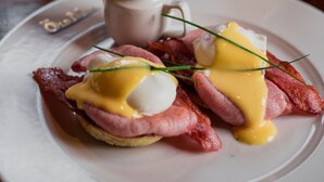 A breakfast plate with eggs Benedict and a glass of orange juice.