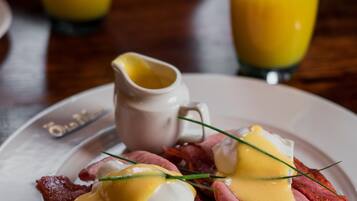 A breakfast plate with eggs Benedict and a glass of orange juice.