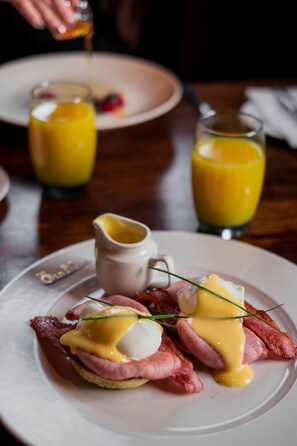 A breakfast plate with eggs Benedict and a glass of orange juice.