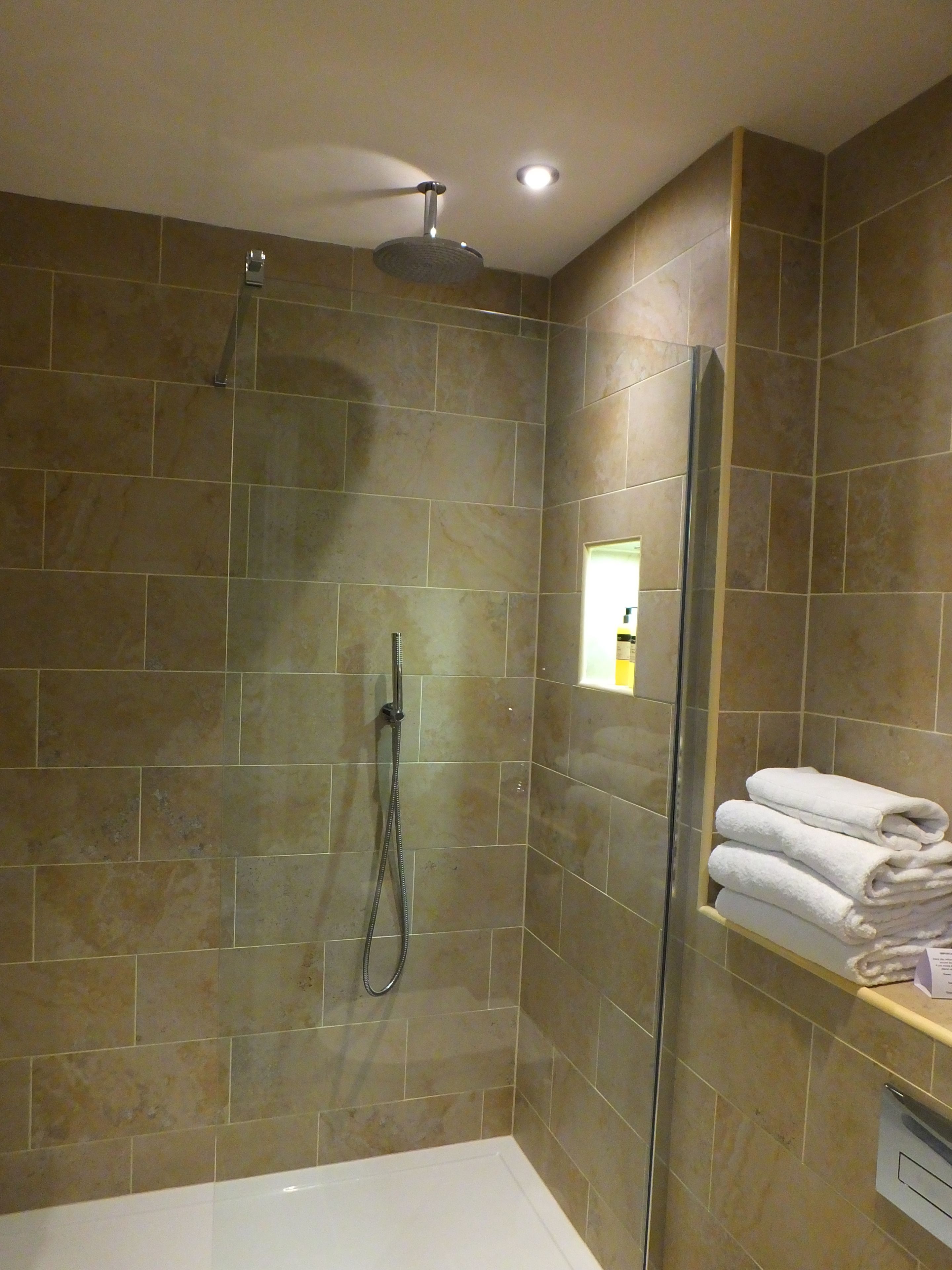 A modern bathroom with a glass-enclosed shower, a white bathtub, and a towel rack with folded towels.