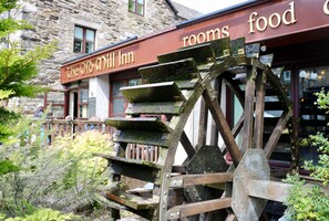 A water wheel in front of The Old Mill Inn, with a sign indicating rooms and food.