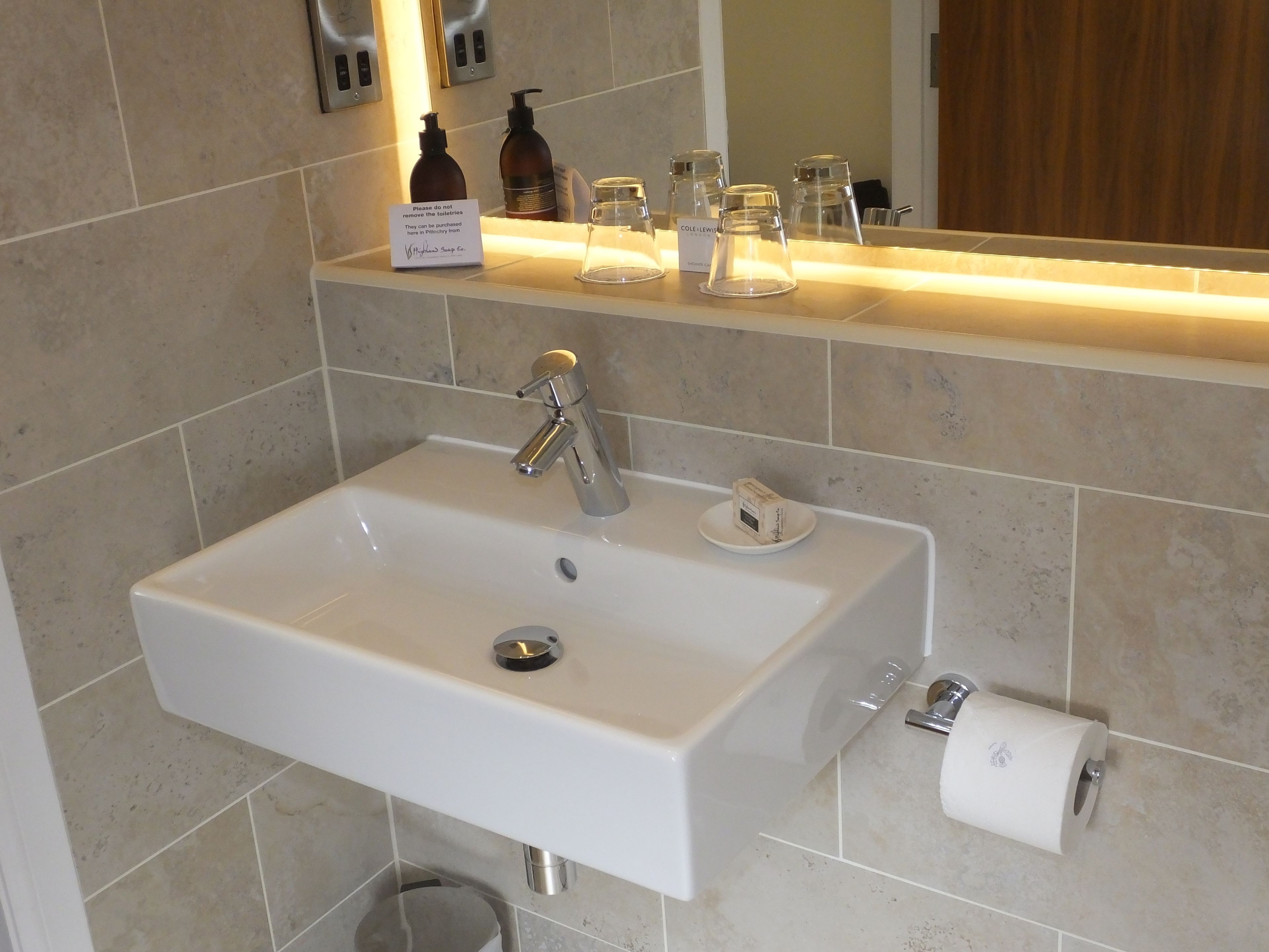 A bathroom sink with a mirror above it, a soap dispenser, and a toilet paper holder.
