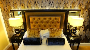A bed with a tufted headboard, two bedside lamps, and patterned wallpaper.
