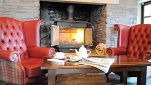 A cozy room with a fireplace, two red leather armchairs, a wooden table with a teapot, cups, and a placemat. - The Old Mill Inn (Pitlochry)
