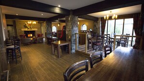A spacious dining area with high ceilings, stone pillars, and large windows. - The Old Mill Inn (Pitlochry)