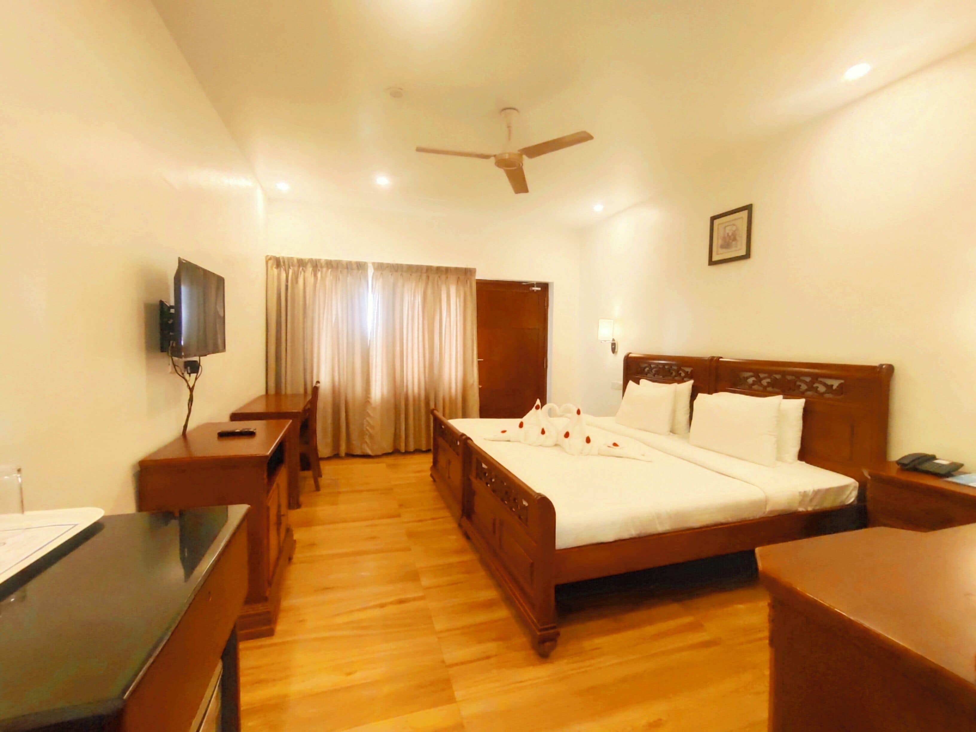 A hotel room with a wooden bed, a desk, a chair, a television, and a ceiling fan.