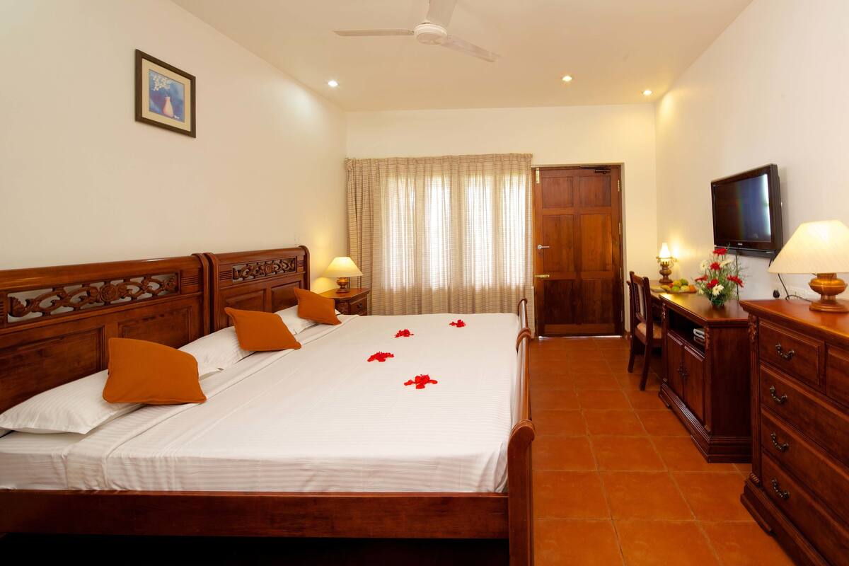 A hotel room with a wooden bed, white linens, a television, a desk, and a chair.