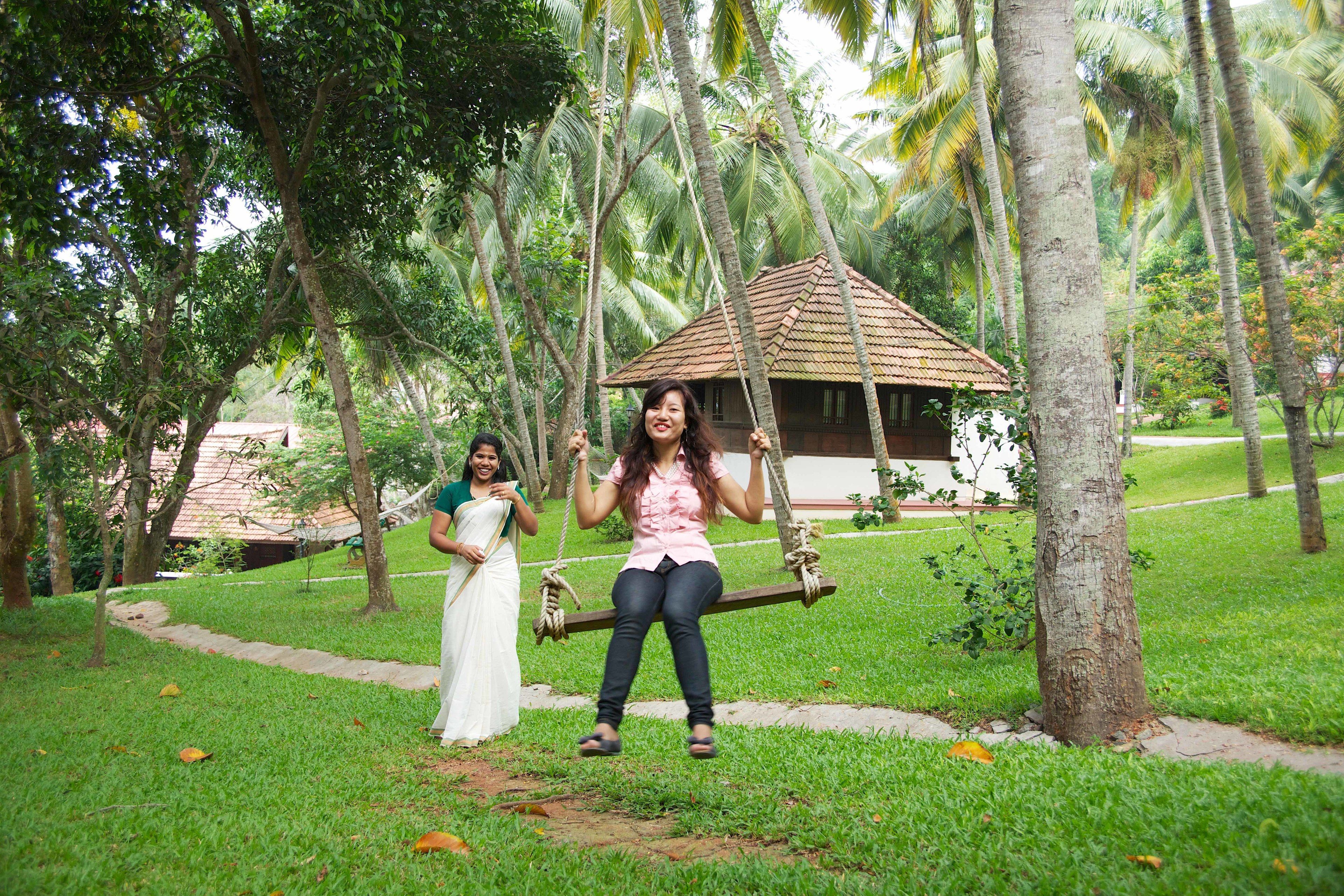 A wooden swing set in a lush garden with a small building in the background.