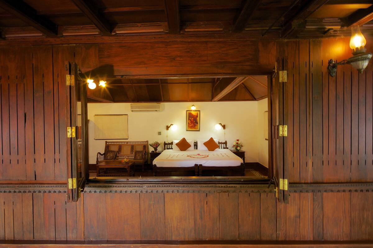 A wooden-framed room with a bed, two wall-mounted lamps, and a painting on the wall.