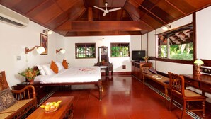 A spacious room with a bed, a desk, and a chair. There is a ceiling fan and a window with a view of greenery outside.