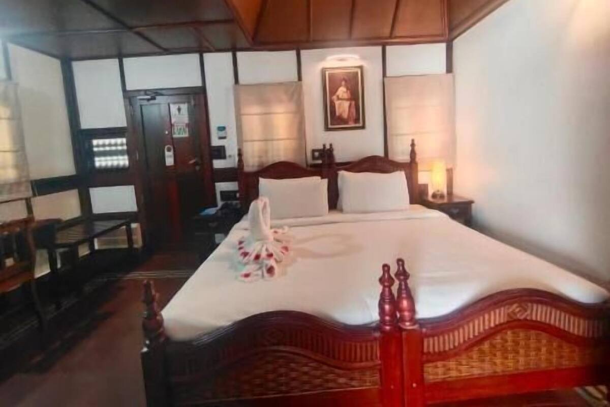 A hotel room with a bed, a nightstand, a lamp, a door, and a wall-mounted picture.