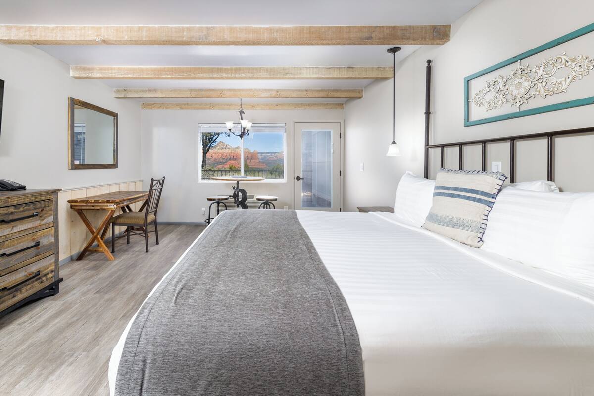 Quarto com cama, escrivaninha e cadeira. Janela com vista para uma montanha.