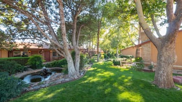 A well-maintained garden with a pond, mature trees, and a clear view of a residential building with a brick facade.