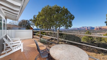 Un patio con sillas Adirondack blancas y una mesa redonda, con vistas panorámicas a montañas y un valle.
