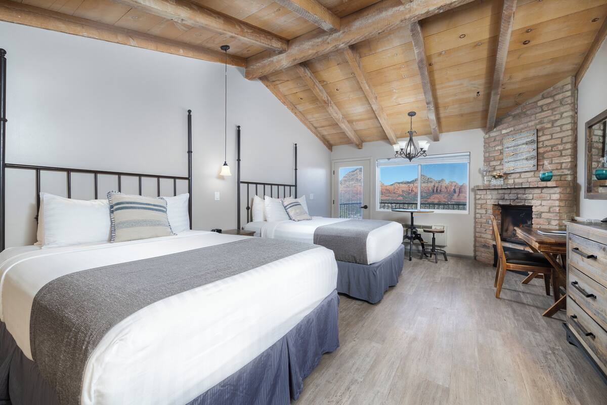 Quarto com duas camas, teto de madeira, lareira e vista para as montanhas.