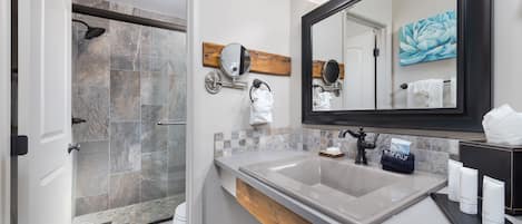 Un baño moderno con ducha, un espejo grande y tocador con artículos de aseo.