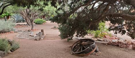 A rustic garden with a wooden pathway, a large tree, and a wooden cart.