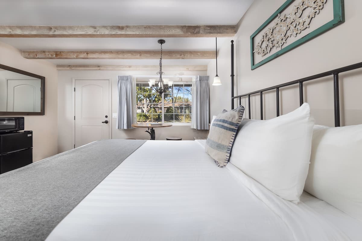 Quarto com cama grande, escrivaninha e janela com cortinas.