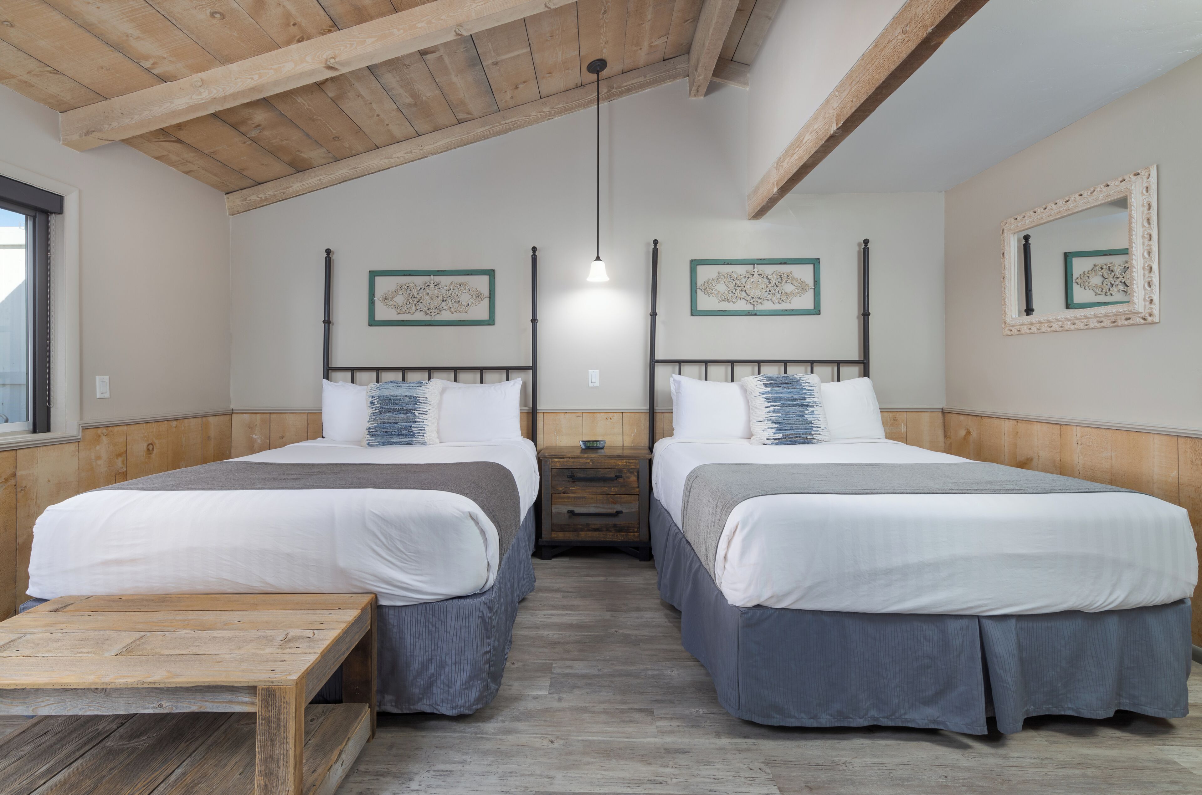 A room with two beds, a wooden table, and a hanging light fixture.