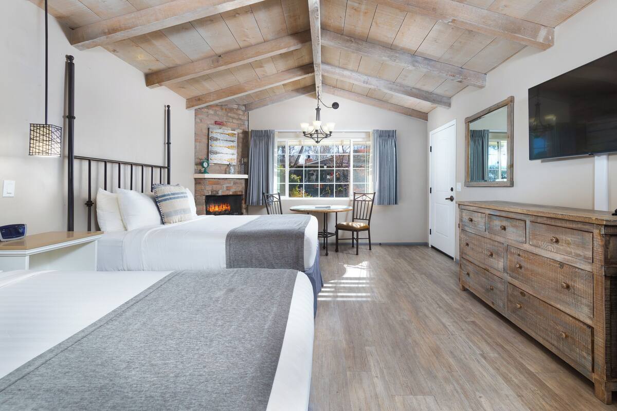 Quarto com duas camas, teto de madeira, lareira, mesa de jantar com cadeiras e televisão.